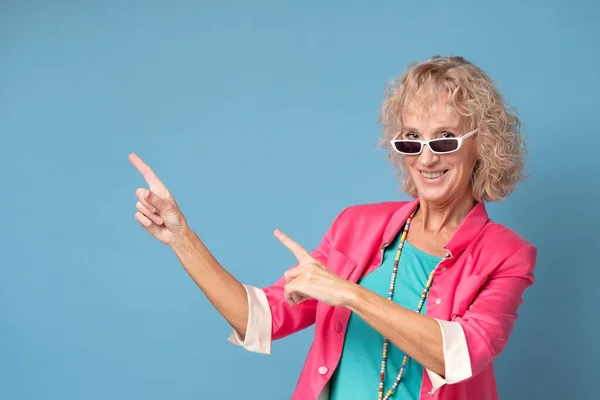 Mujer con gafas de sol sonriendo alegremente y señalando con los dedos delanteros de distancia — Foto de Stock