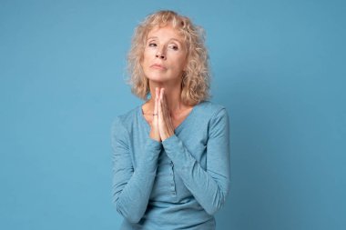 Orta yaşlı beyaz kadın el ele tutuşup samimi bir ricada bulunuyor.