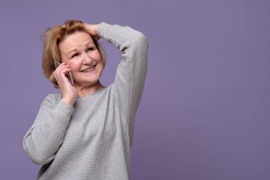 Yaşlı beyaz kadın cep telefonuyla konuşuyor, gülümsüyor, başka tarafa bakıyor.