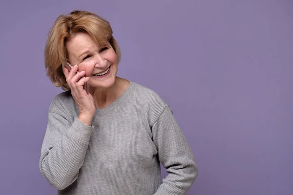 Vieja dama caucásica hablando por teléfono móvil, sonriendo, mirando hacia otro lado — Foto de Stock