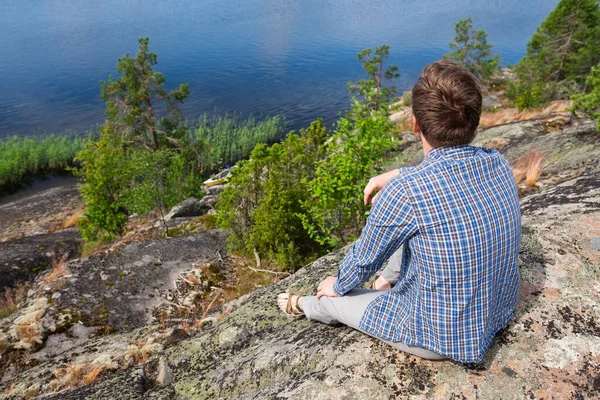 男は湖の近くの石の上に一人で座って田舎の散歩で休息をとる. — ストック写真