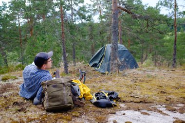 Çadırın yakınındaki açık hava aktivitesinden sonra dinlenen adam gülümseyerek doğanın tadını çıkarıyor..