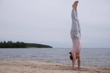 Sahilde amuda kalkarak yoga yapan bir kadın..