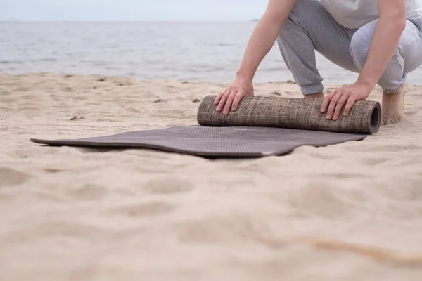 Man rolling up yoga mat after training on sandy beach — Stock Photo, Image