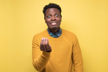 Öfkeli bir Afrikalı arkadaşıyla tartışıyor ve İtalyan jesti yapıyor. Stüdyo fotoğrafı sarı duvarda..