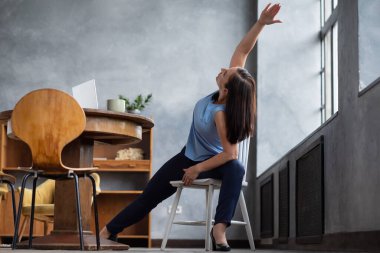 Sandalye kullanarak yoga yapan bir kadın. Genişletilmiş kenar açısı egzersizi yapıyor.