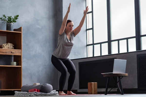 Caucasian woman doing Utkatasana, Chair Pose using block at home — Stock Photo, Image