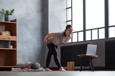 Yoga yapan bir kadın, internetteki ders sırasında Parshvatanasana 'da bacaklarını esnetiyor.