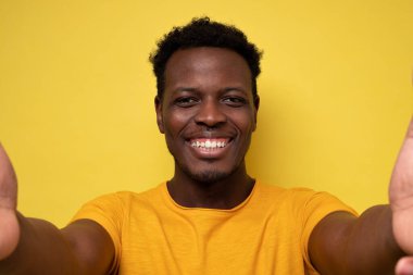 Gülümseyen Afrikalı genç adam sarı arka planda selfie çekiyor.