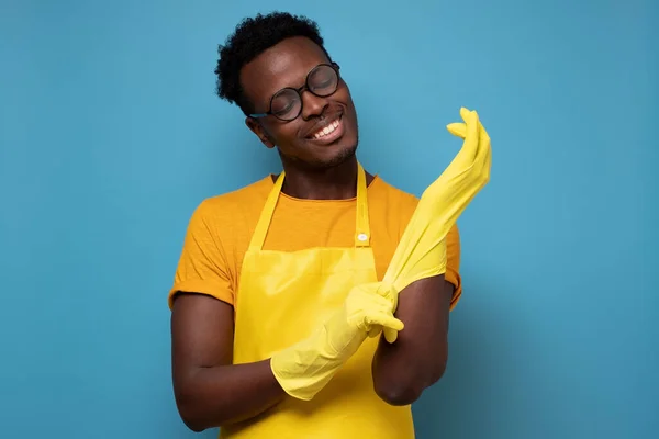 Африканский американец в очках надевает жёлтые резиновые перчатки для чистки. — стоковое фото