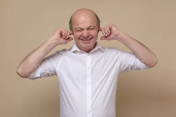 Hombre caucásico mayor cubriéndose los oídos tratando de evitar spoilers auditivos. — Foto de Stock