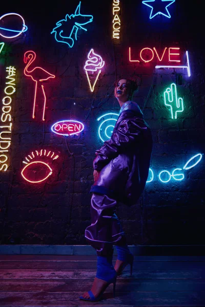 Cyberpunk tiro di modella indossando abbigliamento sportivo contemporaneo contro muro di neon — Foto Stock