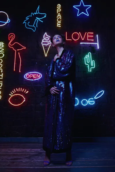 Cyberpunk tiro de modelo vestindo roupão com brilho contra a parede de néon — Fotografia de Stock