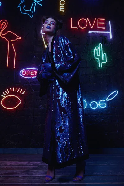 Cyberpunk shooting of model wearing bathrobe with glitter against wall of neon — Stock Photo, Image