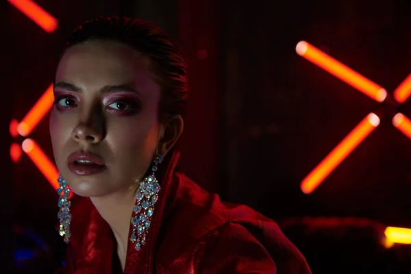 Cyberpunk close up of model wearing red bikers jacket sitting in leather sofa against neon — стоковое фото