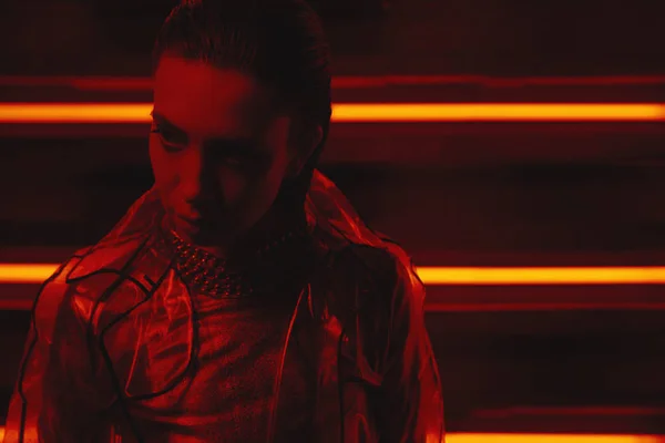 Cyberpunk forgatás modell viselése átlátszó kabátot a celofán és a vörös ruha falán a neon — Stock Fotó