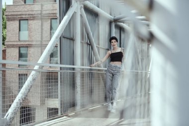 Köprüde poz veren dövmeli kuzgun saçlı genç bayan