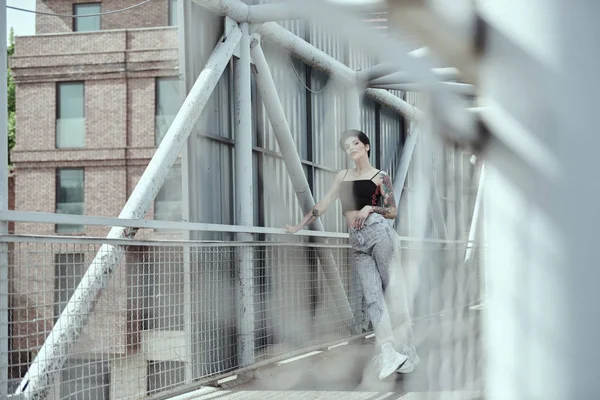 Köprüde poz veren dövmeli kuzgun saçlı genç bayan