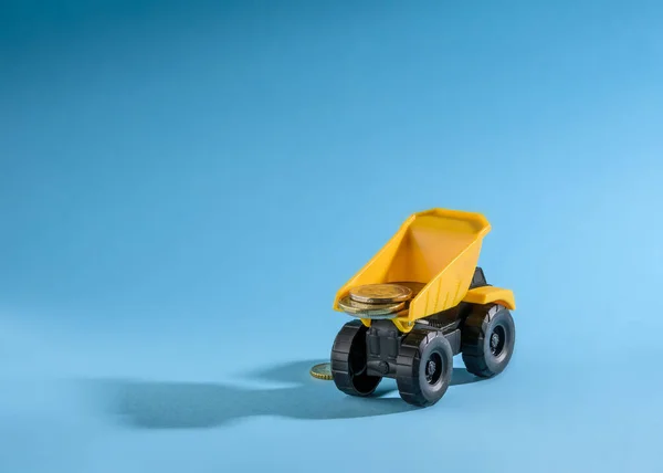 Yellow toy truck loaded with coins money. Space for text. Blue background