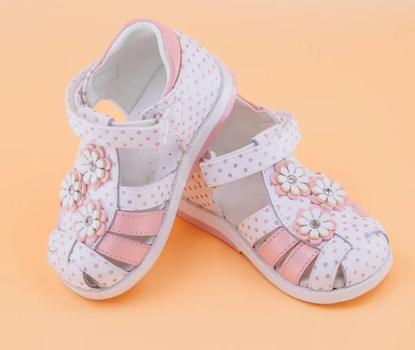 Pair of white sandals in pink peas with white-pink flowers and with clasps fasteners at peach background