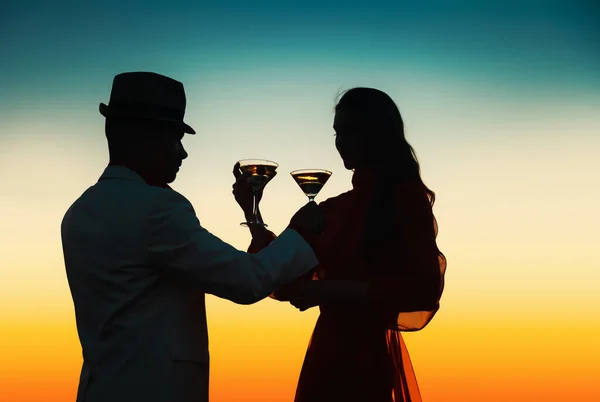 Romantic couple enjoying a glass of wine and beautiful sunset view. Couple drinking glass of cocktail together. Happy life moments. Cheers at sunset.