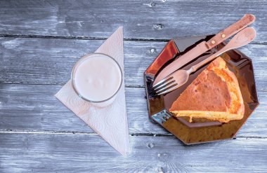 Siyah tabakta bir parça mısır ekmeği, çatal bıçak takımı ve kırsal mavi bir masada bir bardak yoğurt.