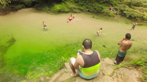 Hombre adulto usando un teléfono móvil en frente de una hermosa encuesta de natación natural — Vídeo de stock