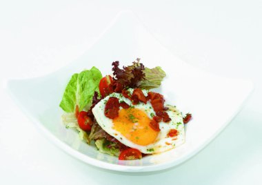 Kızarmış pastırmalı yumurta, roka ve ahşap masada beyaz tabakta domates.