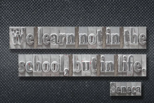 We learn not in the school, but in life - ancient Roman philosopher Seneca quote made from metallic letterpress on dark background
