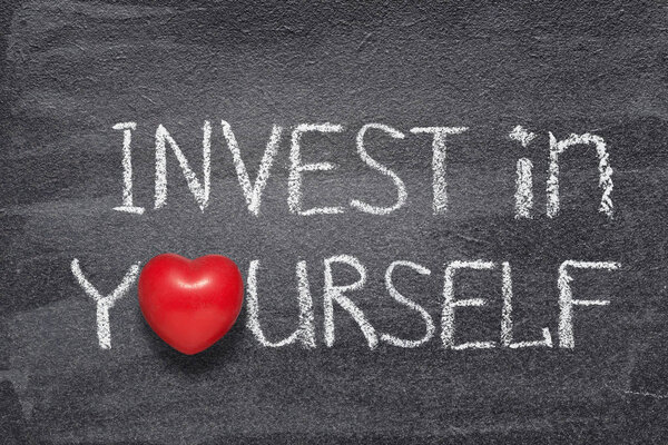 invest in yourself phrase handwritten on chalkboard with red heart symbol instead of O
