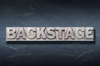 Koyu renk kot pantolon arka grubundaki metal harflerden yapılmış sahne arkası kelimesi.