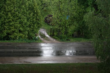 Asfalt Caddesi ve giriş yolu ile güçlü yağmurlu yaz günü yeşil çalılar ile avluda metal kapı