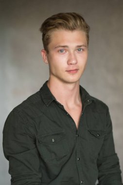 Bir çekim Genç beyaz yakışıklı sarışın adamın gri bir arka plana dayanır.