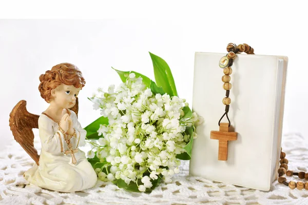 第一圣洁圣餐寂静的生活与天使雕像 木念珠垂悬在祷告书和束百合谷花在白色被隔绝的与处理空间为文本 — 图库照片