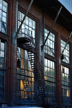 terk edilmiş Tekstil fabrika binası ile büyük pencereler ve yangın kaçış merdiveni günbatımı, Lodz, Polonya 