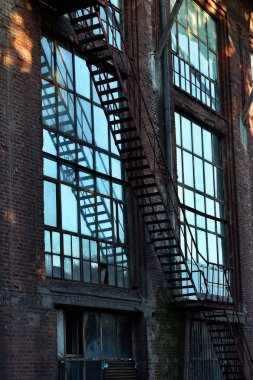 terk edilmiş Tekstil fabrika binası ile büyük pencereler ve yangın kaçış merdiveni günbatımı, Lodz, Polonya