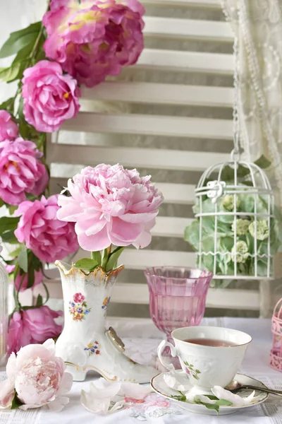 靴の形をした磁器の花瓶でぼろぼろのシックなスタイルのインテリアでフルーツ ティーのカップ新鮮な牡丹の花 — ストック写真