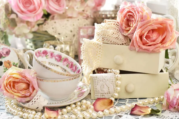 シャビーシックなスタイルのインテリア 磁器紅茶カップ レースとピンクのバラはテーブルの上の小さな引き出しの中 — ストック写真