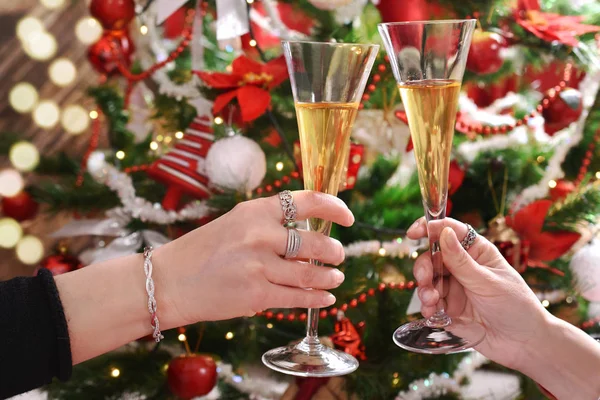 クリスマス ツリーの前にシャンパンのグラスで乾杯をする二人の女性の手 — ストック写真