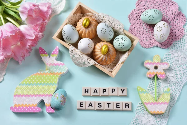 easter flat lay with bunch of pink tulips,painted eggsand mini ring cakes in wooden box and decors on mint background