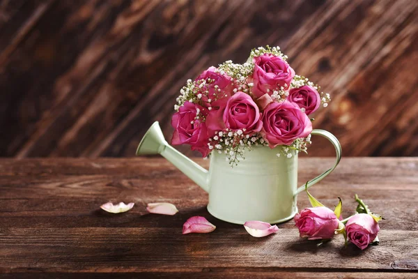 Gäng rosa rosor i en vattna kan på träbord — Stockfoto