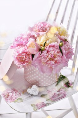 Taze pembe şakayıklar yuvarlak kutuda, benekler beyaz eski moda sandalyenin üzerinde duruyor.