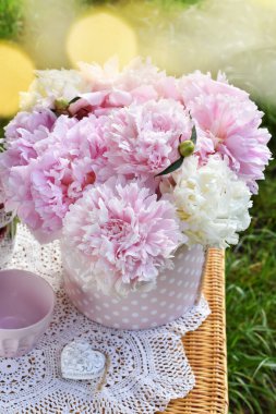 Bir avuç pembe şakayık eski tarz piknik sepeti üzerinde duruyor bahçede çimlerin üzerinde.