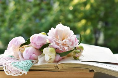 Şakayık çiçekleri ve tomurcuklar bahçedeki masada eski kitapların üzerinde yatıyor.