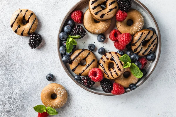 自制肉桂和巧克力迷你甜甜圈的盘子与浆果和薄荷在浅灰色的背板上 — 图库照片