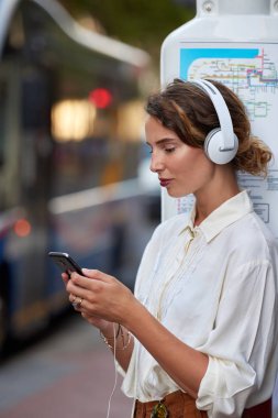 Otobüs durağındaki telefon uygulaması olan bir kadın.