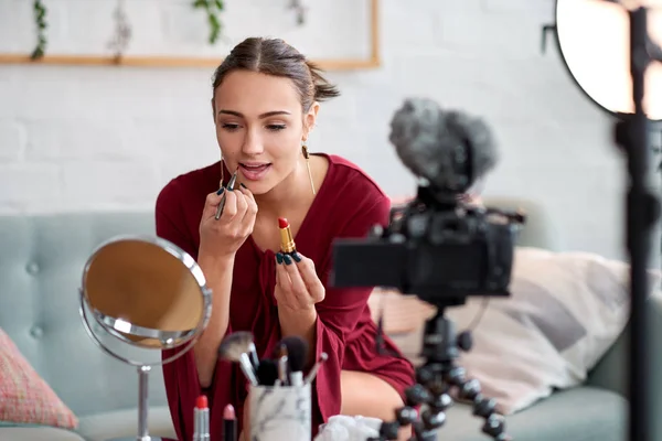 Pretty woman recording video blog vlog and doing make up and applying lipstick