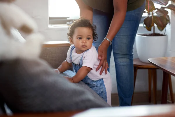 混合种族女婴巡航沿沙发沙发由妈妈支持 学习如何走路移动成长 图库照片