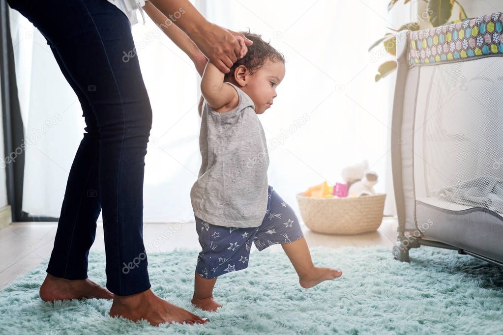 Baby first steps holding mother hands at home