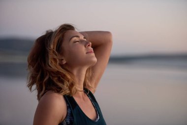 Gözleri kapalı ve başı arkada rüzgarın tadını çıkaran bir kadın.